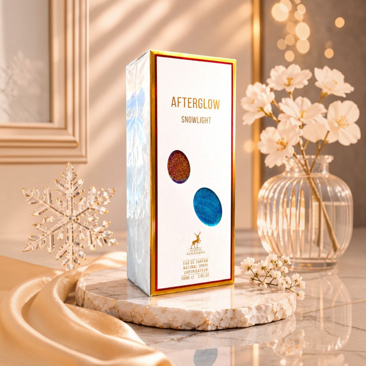 Soghaat Maison Alhambra Afterglow Snowlight 100ml perfume box on a marble stand with white flowers and gold fabric.