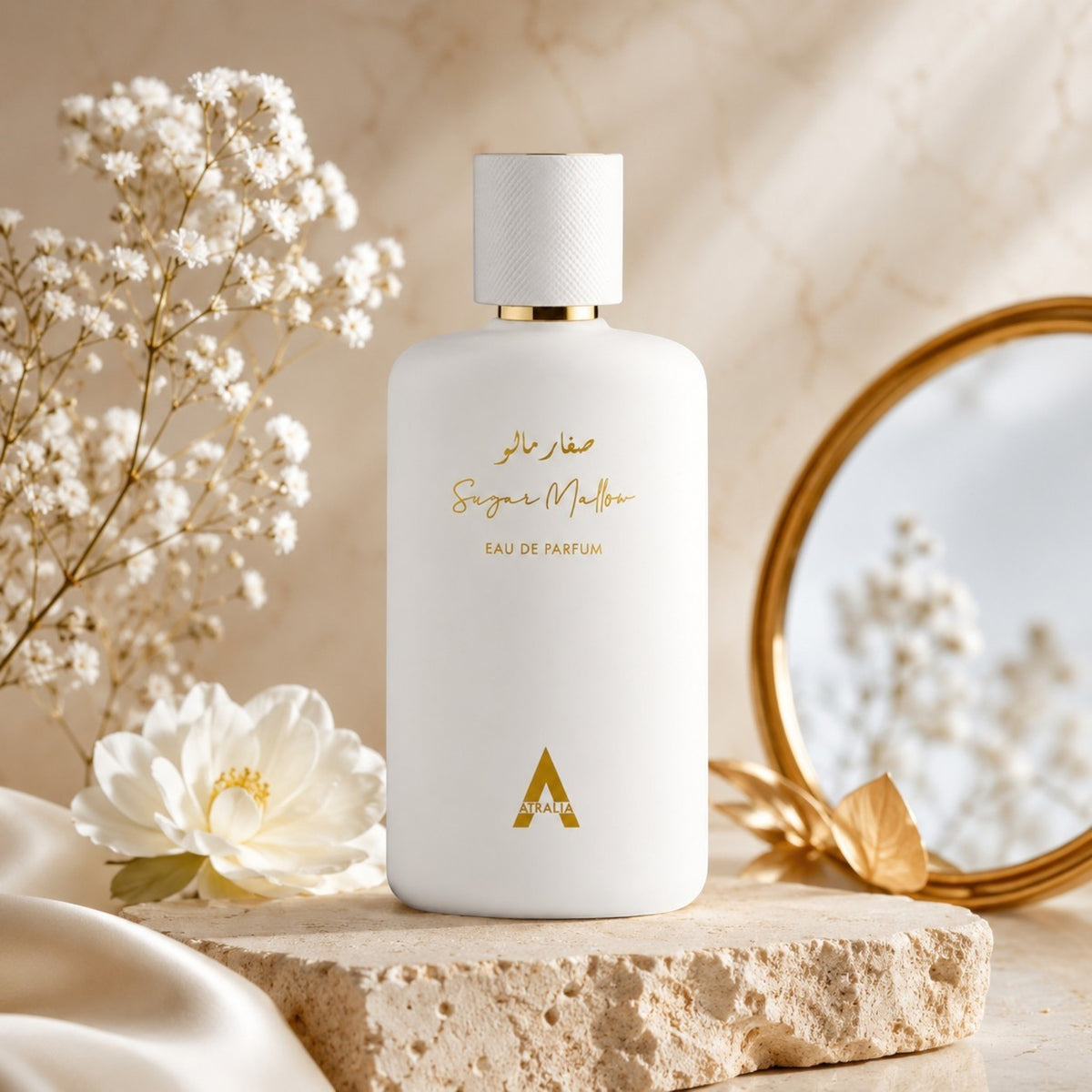 Soghaat Atralia Sugar Mallow Eau de Parfum in a matte white bottle on a stone pedestal with flowers and a gold mirror.