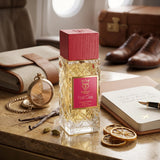 Soghaat Bujairami First Class Extrait de Parfum bottle with a red cap on a desk with travel accessories.