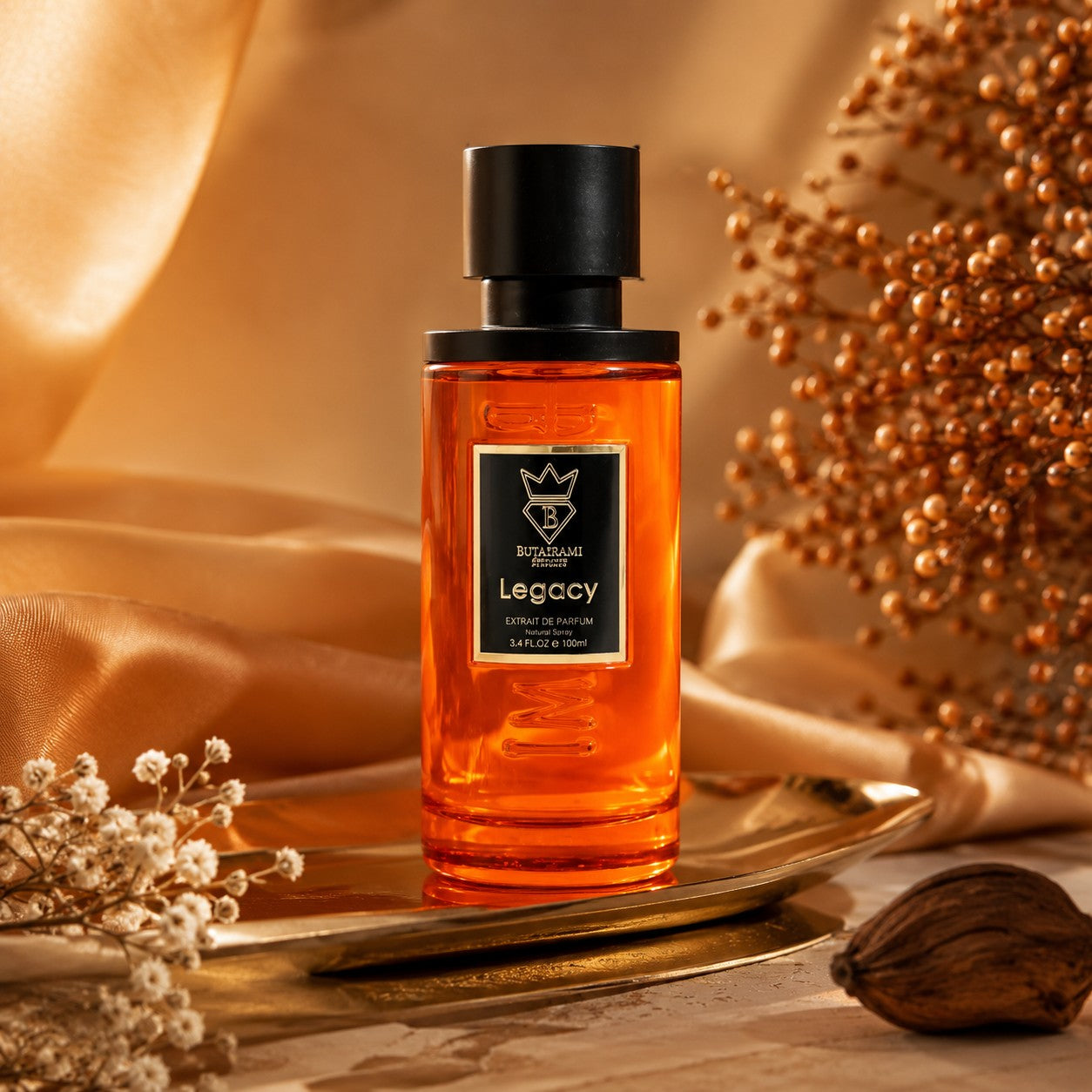 Soghaat Bujairami Legacy 100ml Extrait de Parfum in an amber glass bottle on a gold tray with elegant fabric backdrop.