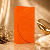 Soghaat Bujairami Legacy 100ml Extrait de Parfum in a vibrant orange box with embossed floral details on a marble surface.
