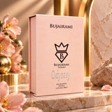 Soghaat Bujairami Odyssey 100ml Eau de Parfum in a soft pink box, displayed on a marble surface with floral accents.