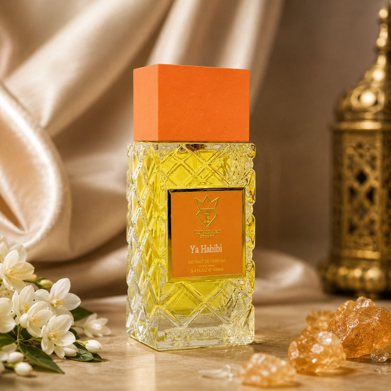 Soghaat Bujairami Ya Habibi Extrait de Parfum in a textured glass bottle with an orange cap, set with white flowers.