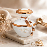Soghaat Dumont Paris Trista Elegance Eau de Parfum in a white and gold bottle with a decorative charm on a marble stand.