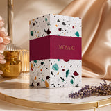 Soghaat Mosaic Extrait de Parfum bottle in a white terrazzo-patterned box with a deep magenta band on a marble surface.