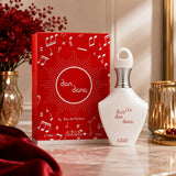 Soghaat Nabeel Dan Dana 100ml Eau de Parfum bottle and red music-themed box on a marble table with red flowers.