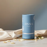 Soghaat Osma Floral A Eau de Parfum in a light blue cylindrical bottle with white floral accents. Notes of ginger, orange blossom, and sandalwood.