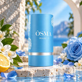 Soghaat Osma Woody F unisex Eau de Parfum in a blue cylindrical bottle, surrounded by blue roses and citrus.