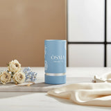 Soghaat Osma Woody W Eau de Parfum in a light blue cylindrical bottle with white floral accents.