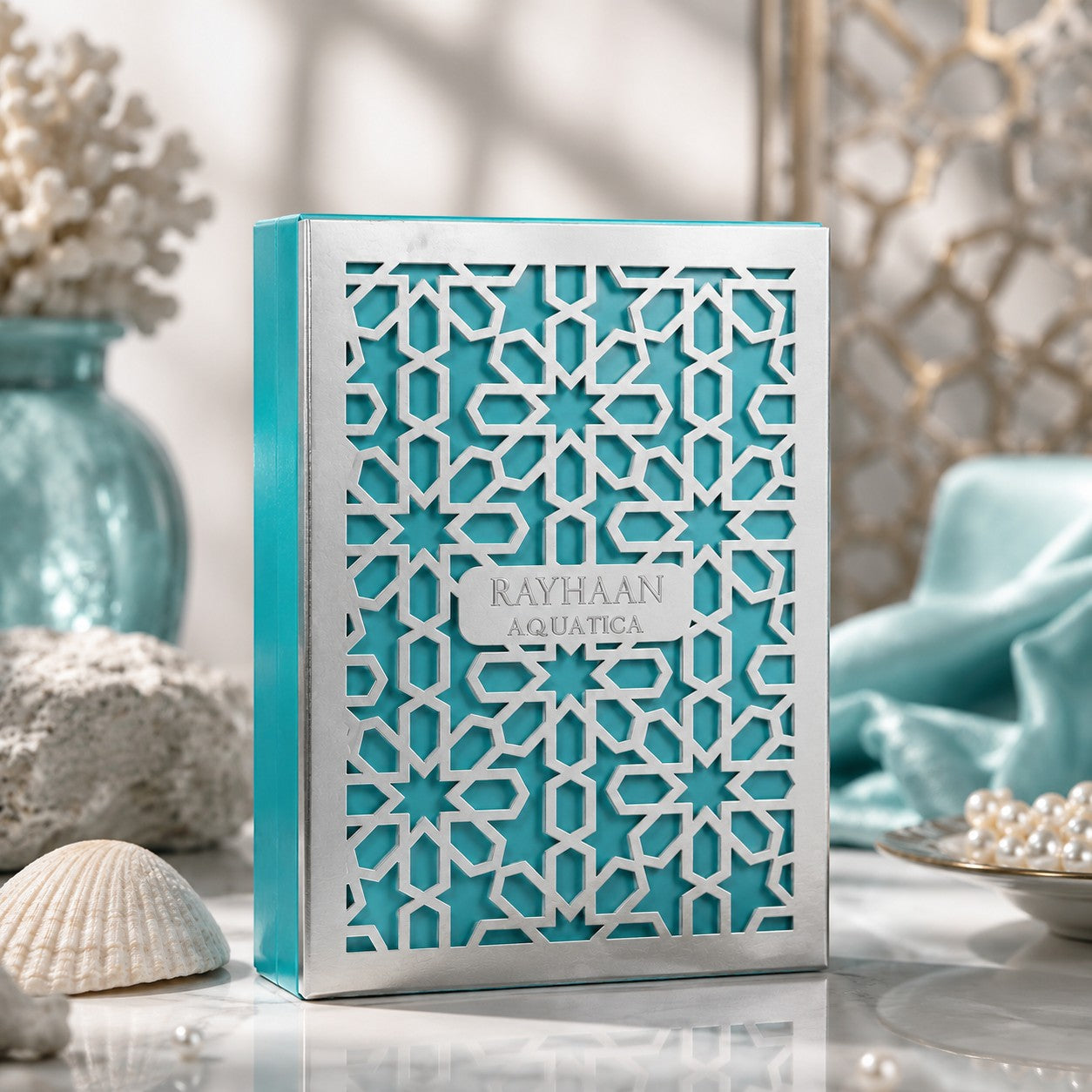 Soghaat Rayhaan Aquatica Eau de Parfum in a teal box with intricate silver geometric lattice, styled with seashells.