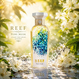 Soghaat REEF Pure Musk unisex Eau de Parfum bottle surrounded by white flowers and water splashes in sunlight.