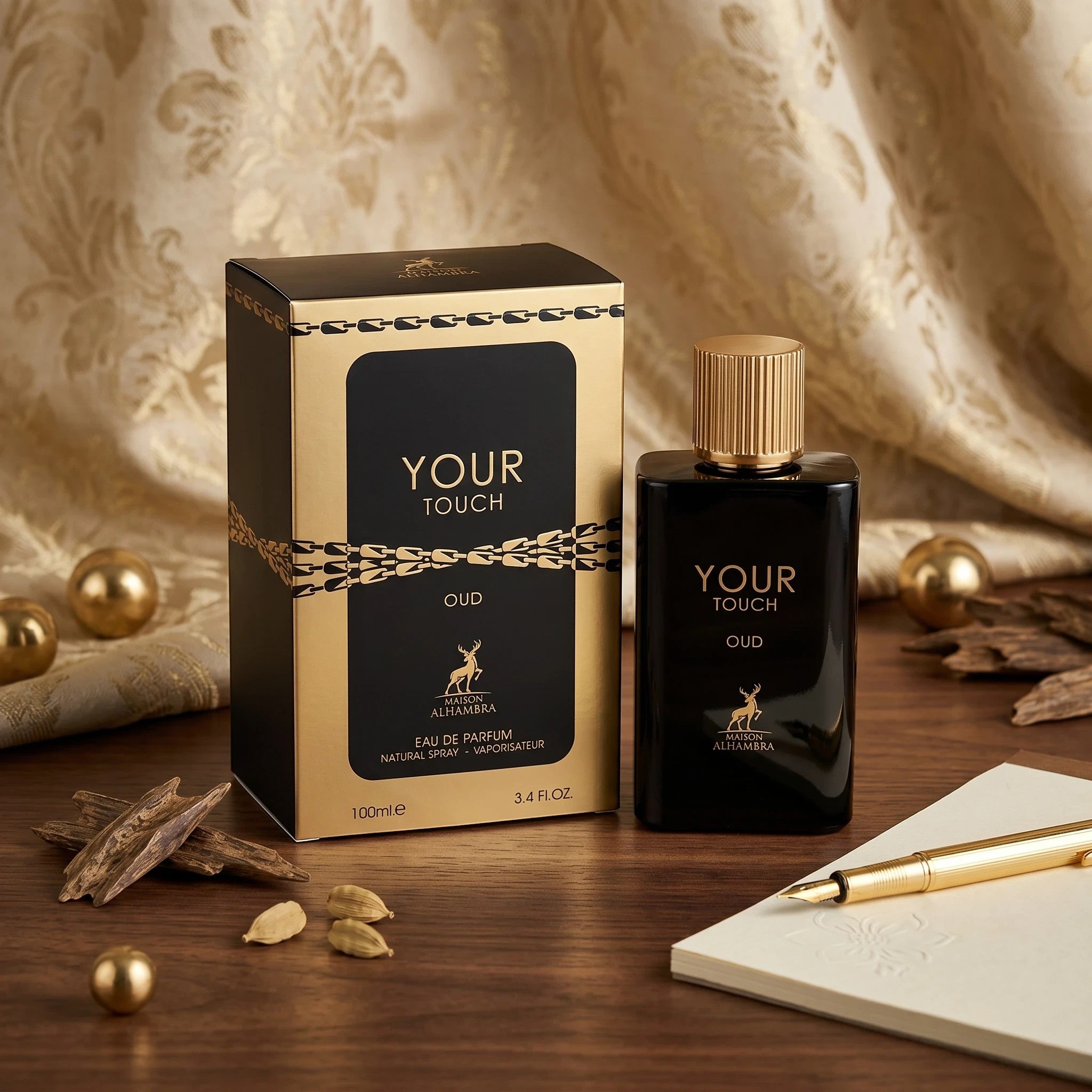 Soghaat Maison Alhambra Your Touch Oud 100ml Eau de Parfum bottle and box with gold accents on a wooden desk.