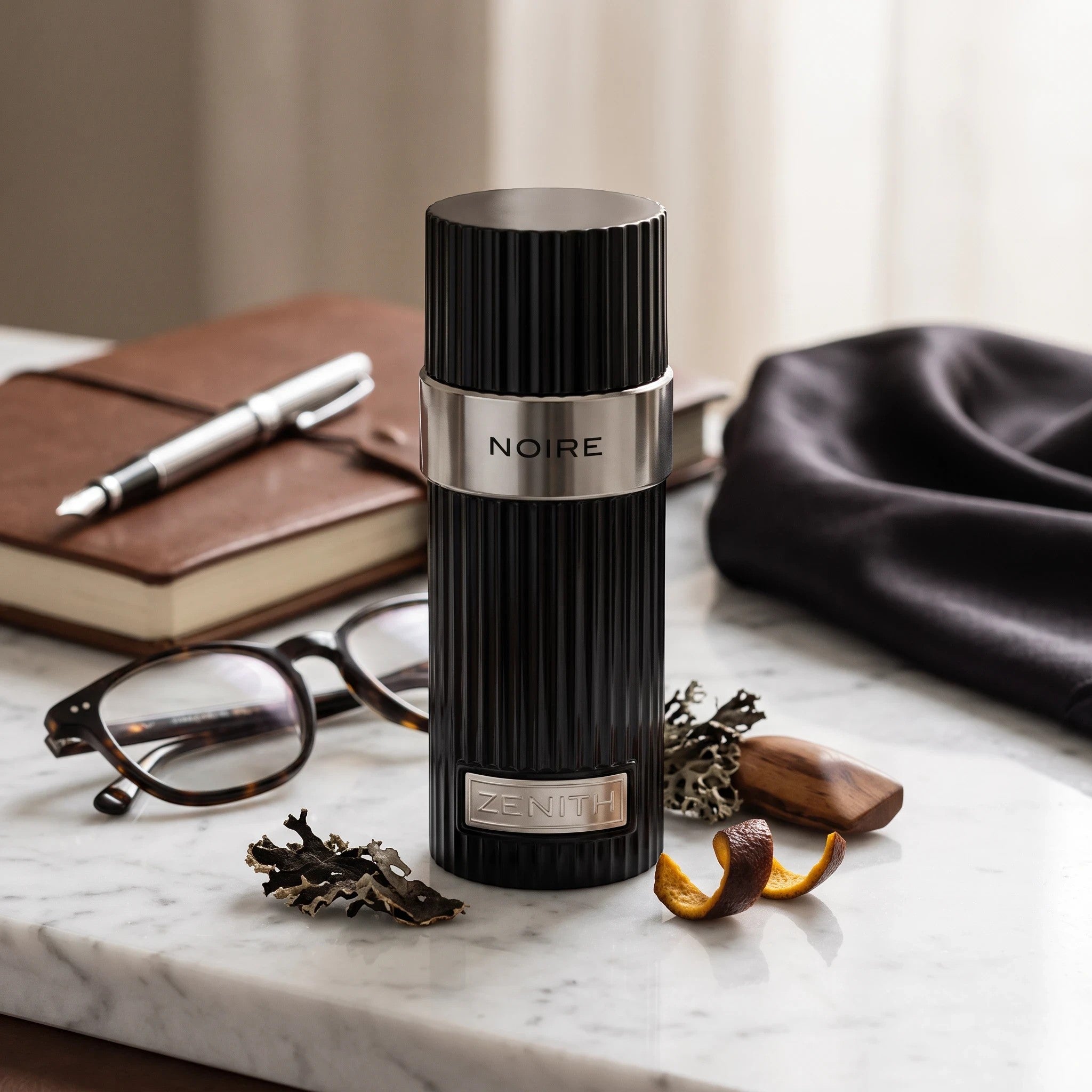 Soghaat Zenith Noire Eau de Parfum, a sleek black ribbed bottle with silver accents on a marble desk with accessories.